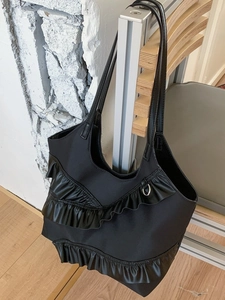 Black ruffles shoulder tote bag with lace-edge bow design hanging on a minimalist chair