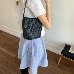 Minimalist black woven bucket bag for women with leather texture and slim shoulder strap