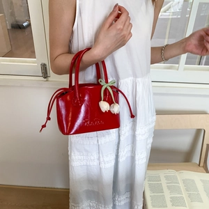 Detail of red glossy bucket bag with tulip charms and a light green silk bow decoration