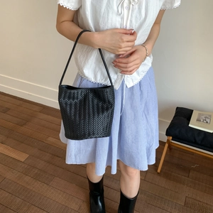 Detailed view of black woven bucket bag with long shoulder strap in a minimalist setting