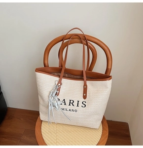 Detail of woven straw tote bag with brown leather handles and star charm on a wooden chair