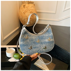 Dettaglio borsa a mezzaluna in denim azzurro con decorazioni a farfalla d'argento