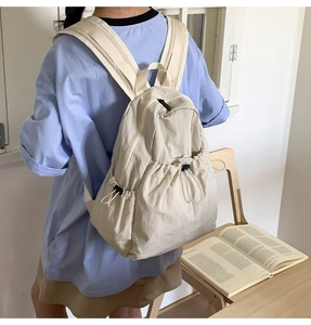 Detail of beige nylon pleated drawstring backpack with wide straps in casual setting