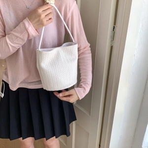 Detail of the white woven bucket bag showing intricate V-pattern texture and shoulder strap
