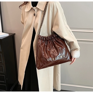 Detail of dark brown quilted drawstring bag with chain strap and heart logo on trench coat