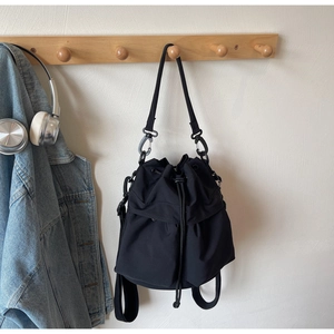 Detail of a black nylon drawstring bucket bag with metal hooks on a wooden wall