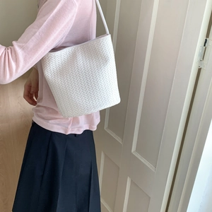 Detailed view of white woven bucket bag showing textured pattern and shoulder strap