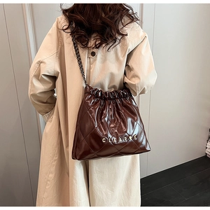 Detail of dark brown quilted shoulder bag with chain strap worn with a beige trench coat