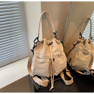 Detail view of cream drawstring bucket bag with shiny nylon fabric and woven strap