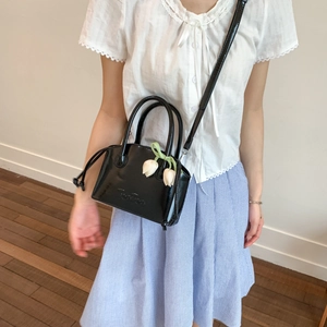 Close-up of black patent leather crossbody bag with a white tulip flower pendant charm
