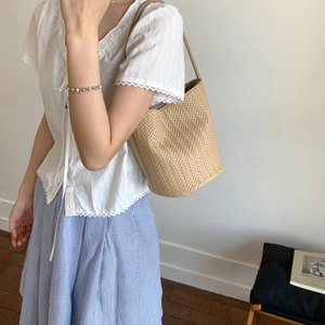 Detail of woven straw bucket bag showing herringbone pattern and slim leather strap