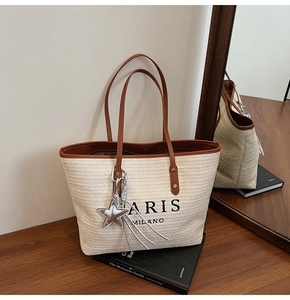 Detail of woven straw tote bag featuring leather handles and Paris Milano embroidery