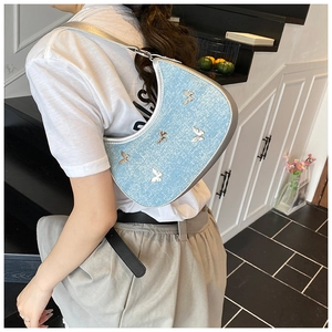 Dettaglio della borsa a mezzaluna in denim con farfalle argentate indossata da modella