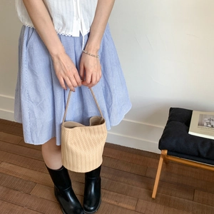 Close-up of beige woven bucket bag featuring a V-shaped texture and long leather handles