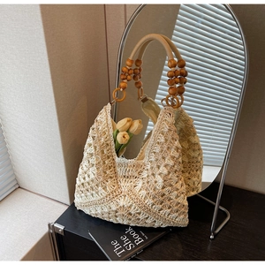 Detail of woven straw tote bag featuring round wooden beads handle and floral texture