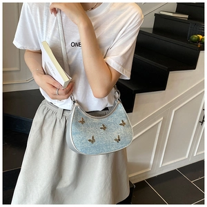Dettaglio borsa hobo celeste glitterata con ciondoli a farfalla indossata da modella