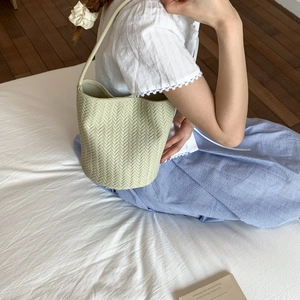 Detail of light green woven bucket bag with herringbone texture and slim shoulder strap