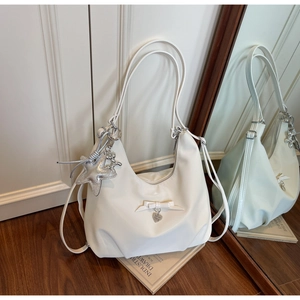 Detail of a white crescent shoulder bag featuring a stylish bow and cute hanging charms