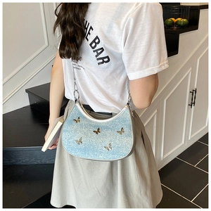 Dettaglio della borsa a mezzaluna in denim celeste con farfalle metalliche sulla tracolla