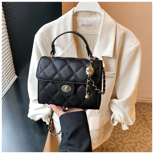 Detail of black quilted leather handbag with gold rotating lock and chain strap ornament