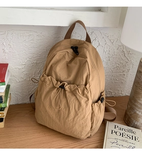 Detailed view of a light brown nylon pleated backpack with drawstring front pocket and wide handle