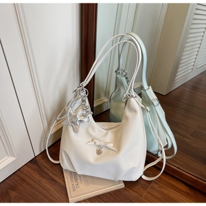 Detail of cream shoulder bag with star charm and bow pendant on wooden floor background