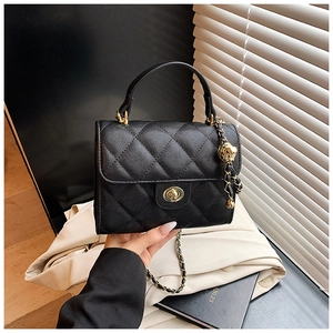 Detail of black quilted leather handbag featuring a golden lion head charm and chain strap