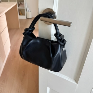 Close-up of black pleated cloud bag with thick braided rope knot handles and silver metal rings