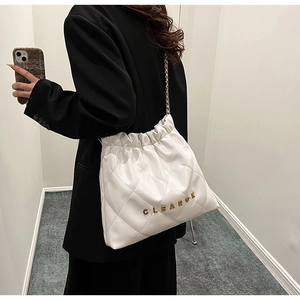 Detail of white quilted bucket bag with gold metal letters and chain strap on shoulder