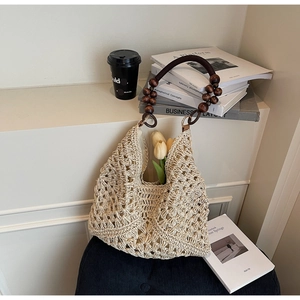Detailed texture of hollow knit beige tote with round wooden bead handles on a chair