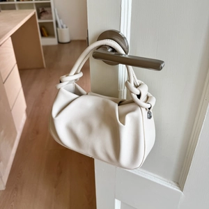 Detail of ruched cream leather bag with knot handle hanging on a door handle