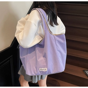 Detail einer großen lila Canvas-Tasche mit gewebtem Etikett und breitem Schultergurt