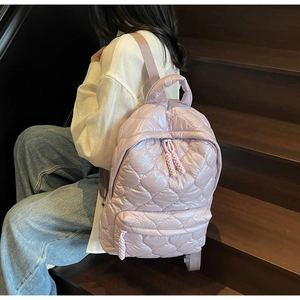 Detailed view of heart-quilted lavender backpack worn by a model on wooden stairs