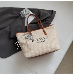 Detail of woven straw tote bag with brown leather trim and Paris Milano print