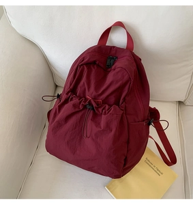 Detail of burgundy drawstring backpack with pleated nylon texture on a cream sofa