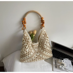 Detail of hand-woven hollow knit tote bag with wood bead handles on white bedding
