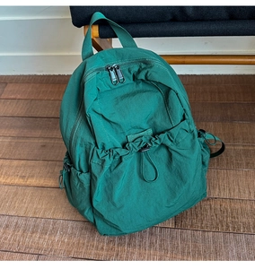 Detailed view of dark green nylon drawstring backpack featuring pleated fabric on wood floor