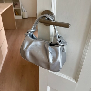 Detail of silver metallic dumpling bag with knotted handle and pleated texture design