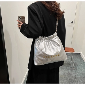 Close-up of silver quilted bucket bag with chain strap and gold metallic logo lettering