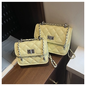 Detail of yellow quilted leather crossbody bags with metal chain straps on a wooden table