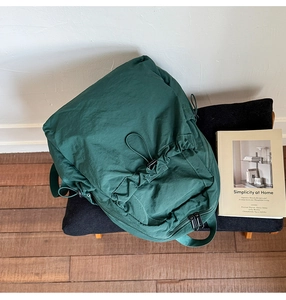 Detail of dark green nylon drawstring backpack with pleated texture on a black bench