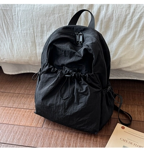 Detail of black nylon backpack featuring drawstring pocket and wrinkled fabric texture