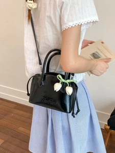 Chic black patent leather crossbody bucket bag with elegant white tulip floral accessory