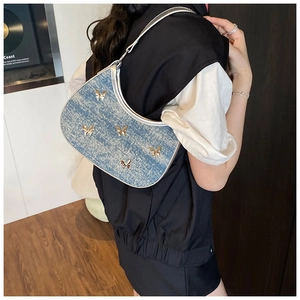 Dettaglio borsa hobo in denim con finiture argento e farfalle dorate sulla modella