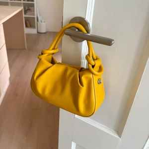 Detail of yellow pleated cloud bag with knotted handle hanging on a white door