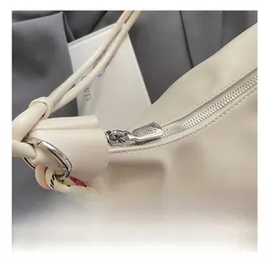 Detalle de cremallera plateada y cuerda trenzada en un bolso de cuero beige