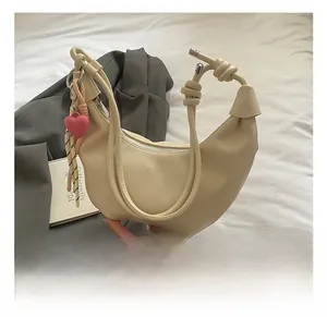 Detalle de bolso medialuna beige con asas anudadas y colgante de corazón rosa