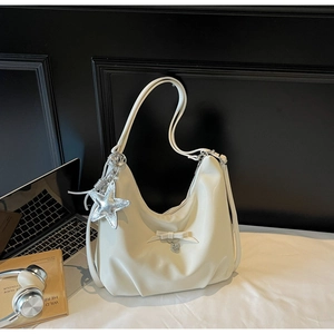 Detail of hobo bag featuring decorative bow, star charm, and heart pendant on cream fabric