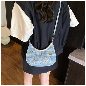 Dettaglio borsa a mezzaluna in denim blu con farfalle metalliche dorate sulla modella