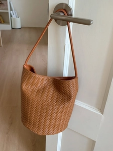 Brown woven bucket bag with long shoulder strap displayed on a door handle